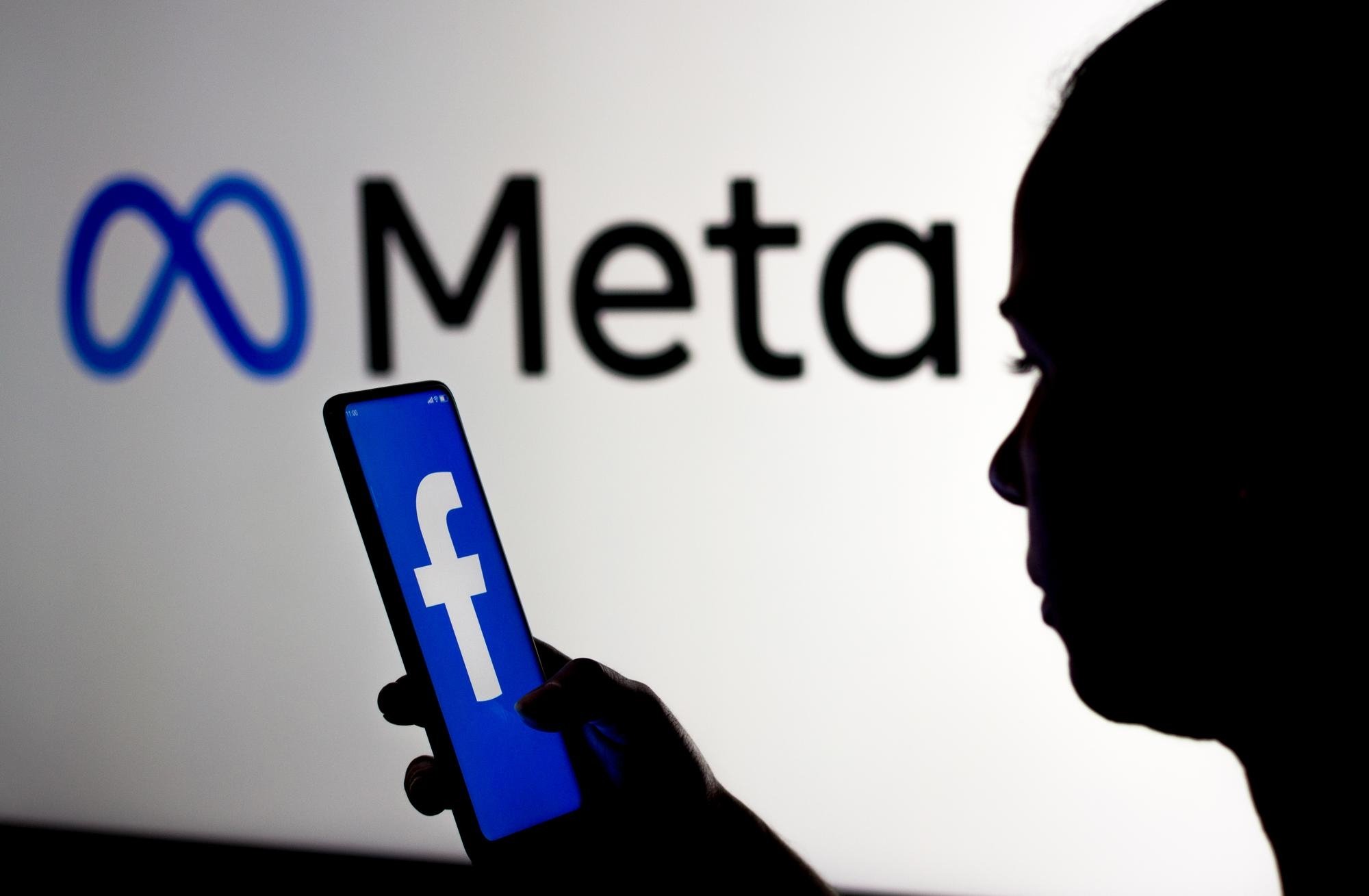 Pessoa a usar smartphone com o facebook aberto e o logo da Meta em fundo